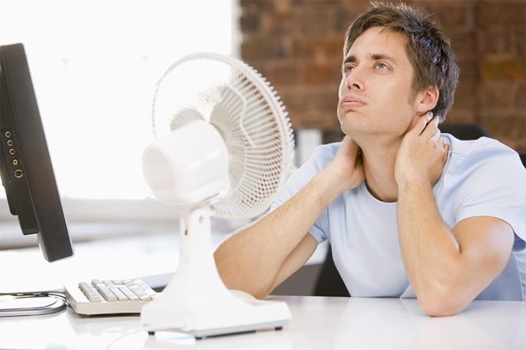 Man in office with computer and fan cooling off